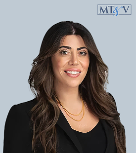 Portrait of a smiling woman with long dark hair, wearing a black blazer and gold necklace, against a light blue background with the MTSV logo in the corner. Chanel  Miller, Tischler & Vislosky, P.C. Chanel  Miller, Tischler & Vislosky, P.C.