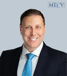 Smiling man in a navy suit and blue tie against a light blue background, MT SV logo in the top-right corner. brett  Miller, Tischler & Vislosky, P.C. brett  Miller, Tischler & Vislosky, P.C.